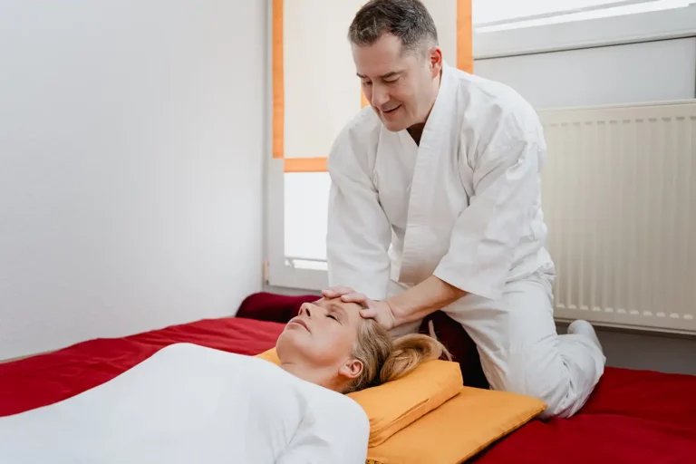 Therapeut in Shiatsu-Anzug behandelt liegende Patientin am Kopf