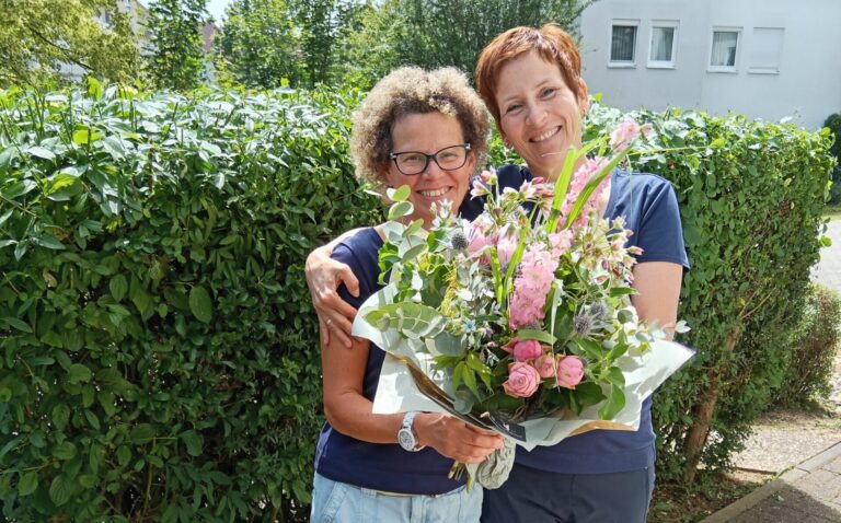 Zwei Mitarbeiterinnen mit Blumenstrauß in Hand.